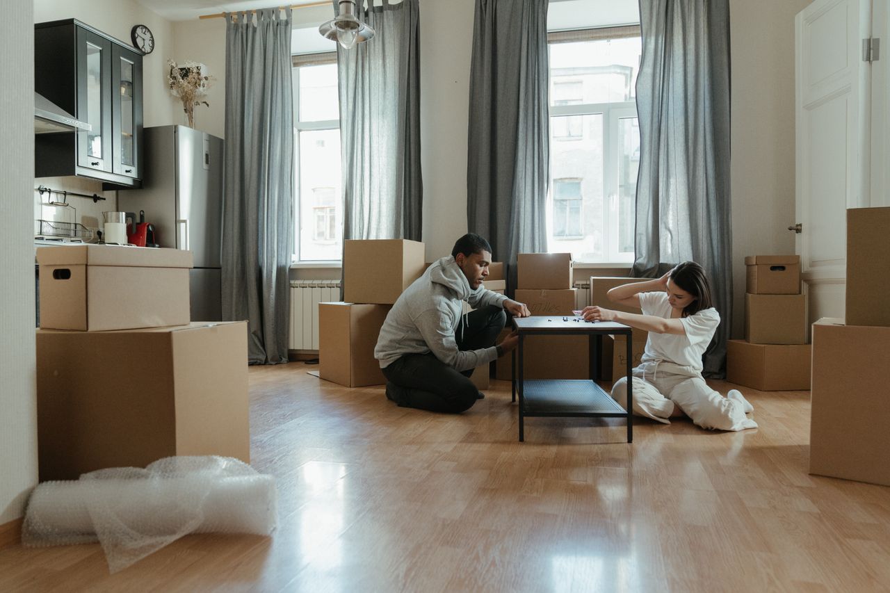 why-choose-us-03 Young couple assembling furniture in their new apartment, surrounded by cardboard boxes.