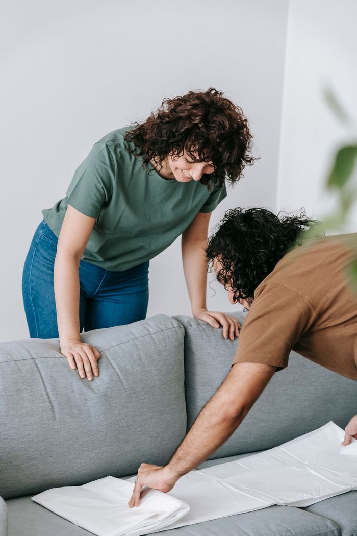 hero-02 Couple preparing living room by covering the couch with protective white cloth.