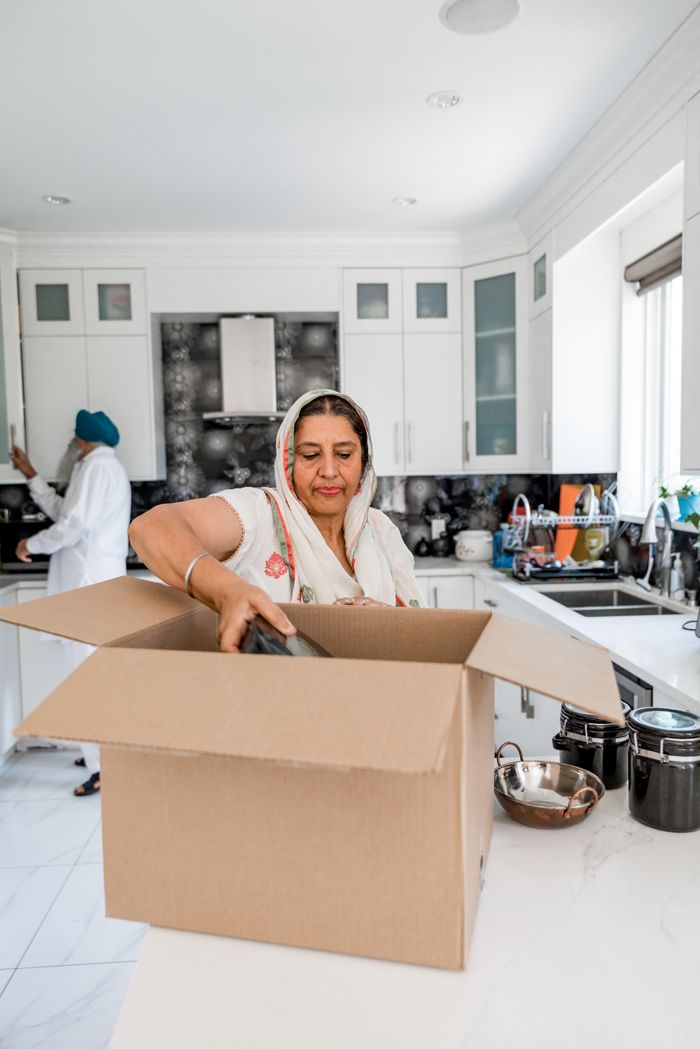 hero-01 A woman unpacks cardboard boxes in a bright, modern kitchen setting.
